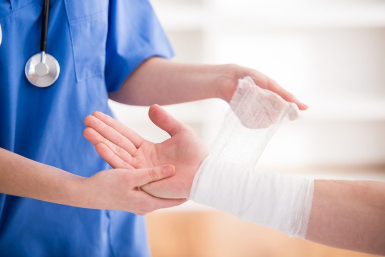 Close-up female doctor is bandaging upper limb of patient.